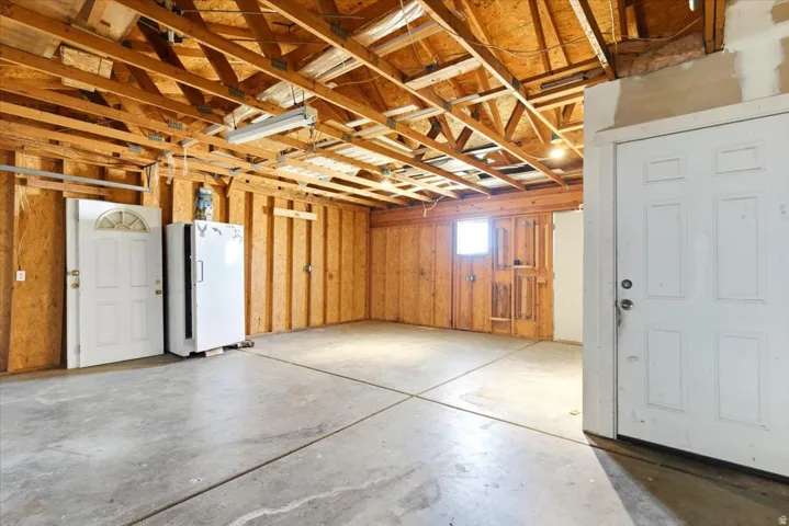 Spacious utility room featuring a concrete floor, exposed wooden ceiling joists, wood-paneled walls, and two white panel doors