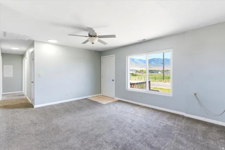 Carpeted interior with light gray walls, a ceiling fan, and a large window offering mountain scenery