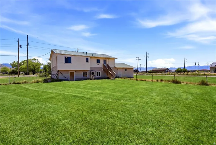 Expansive green lawn with a white exterior structure featuring a green metal roof and a wooden exterior staircase