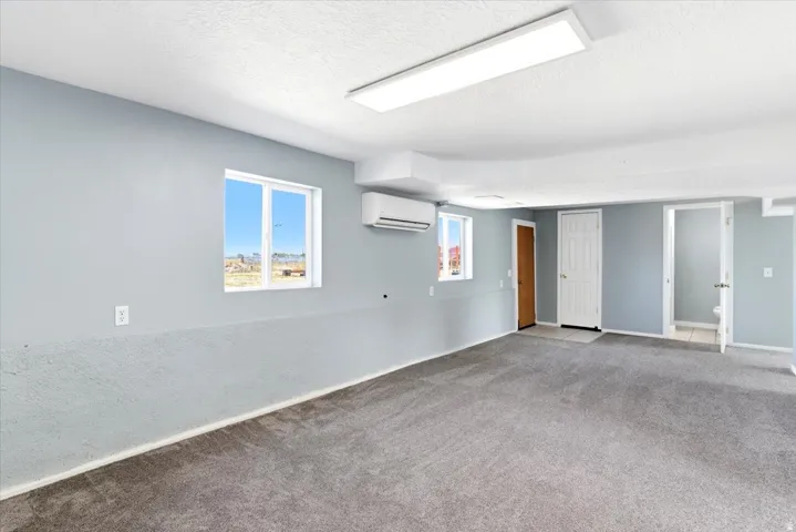 Spacious room featuring light gray walls, textured lower wall paneling, and dark gray carpeting