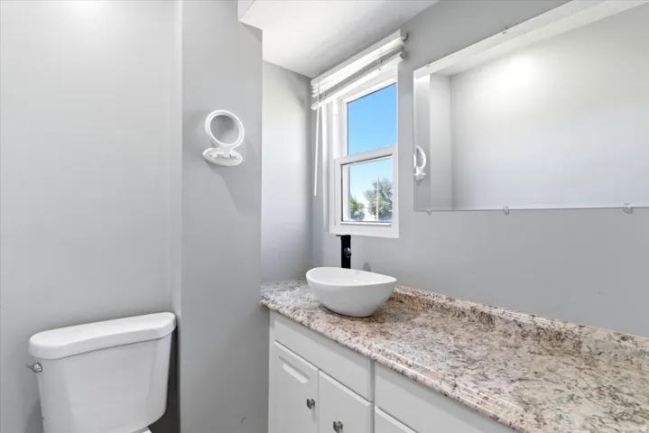 Bathroom featuring a vanity with a vessel sink, light-toned countertop, and white cabinetry