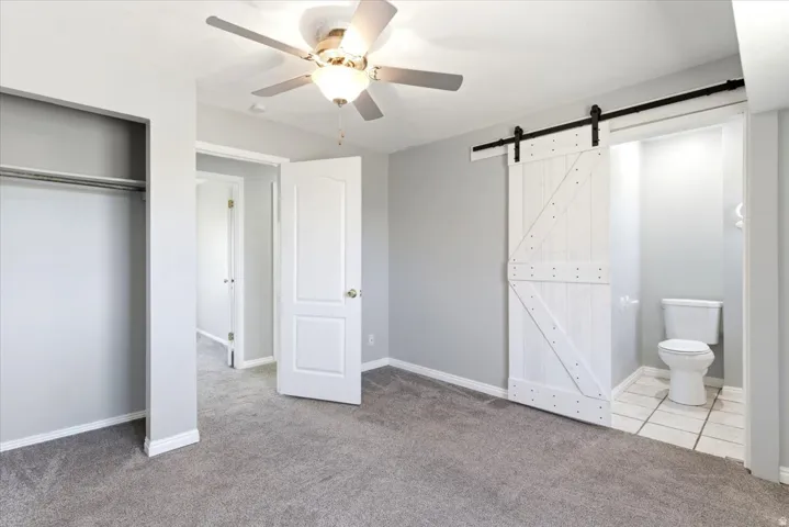 Bedroom featuring gray carpeting, a ceiling fan, and a white barn door