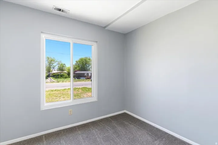 Interior room featuring light gray wall paint, a white-framed sliding window, and neutral-toned carpeting