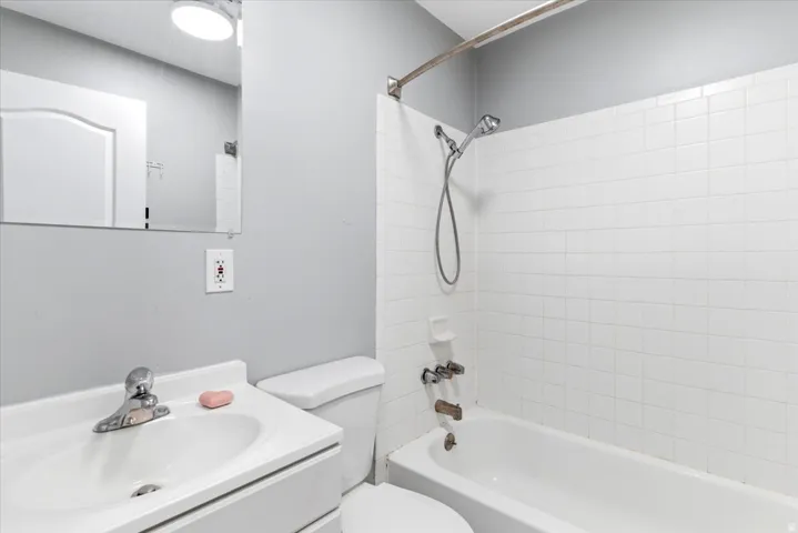 Bathroom featuring a vanity with an integrated sink, a commode, a shower/tub combination with white subway tile surround, and a wall-mounted mirror