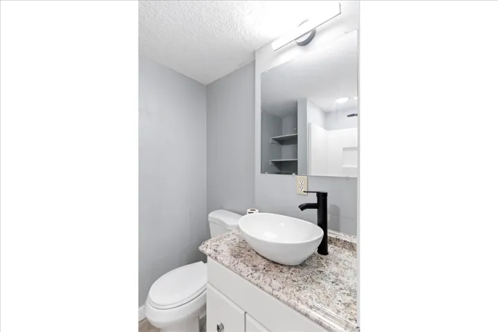 Modern bathroom featuring a vessel sink, dark-finish faucet, granite-style countertop, and vanity mirror with integrated lighting