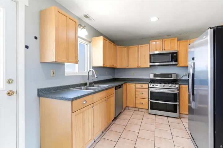 Kitchen featuring natural wood cabinetry, stone-finish countertops, and stainless steel appliances