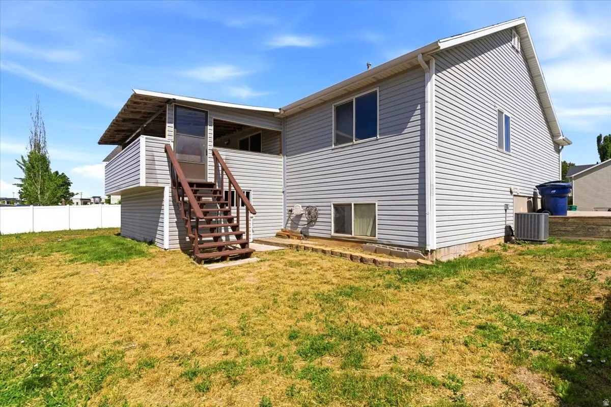 Rear exterior featuring light gray siding, a second-story balcony with a brown wood-finish staircase, and multiple windows