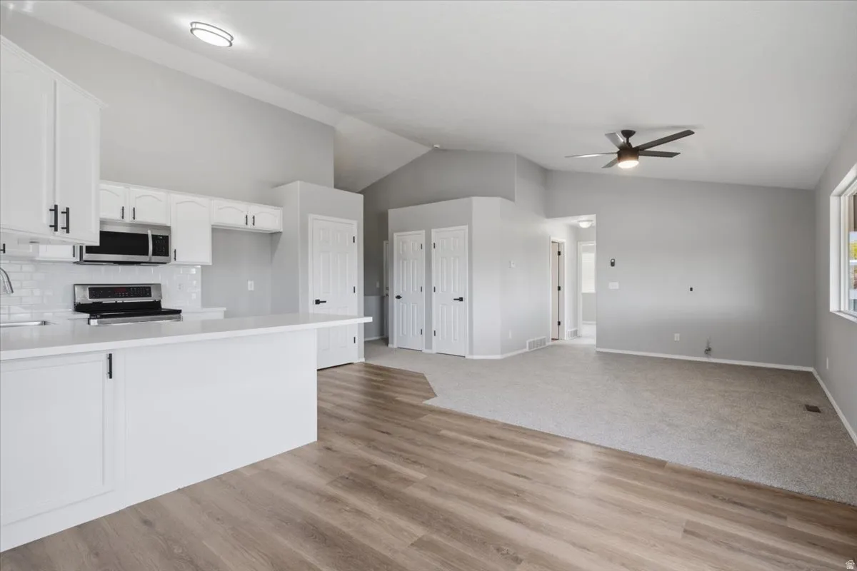 Vaulted ceilings above a kitchen with white cabinetry, a subway tile backsplash, and a built-in microwave