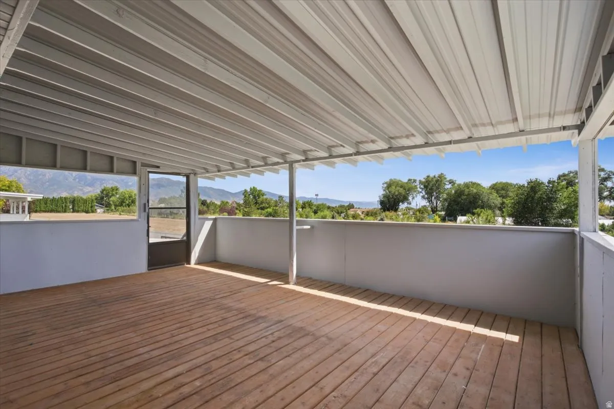 Covered outdoor deck with wood-finish flooring, white perimeter walls, and a screen door