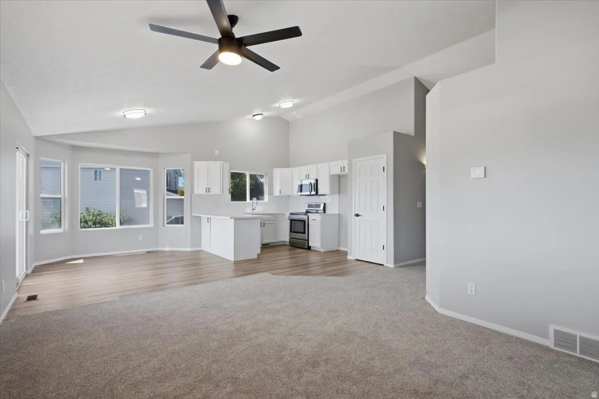 Vaulted ceilings, a contemporary ceiling fan, and recessed lighting illuminate this open-concept room with light wood-finish flooring and carpet