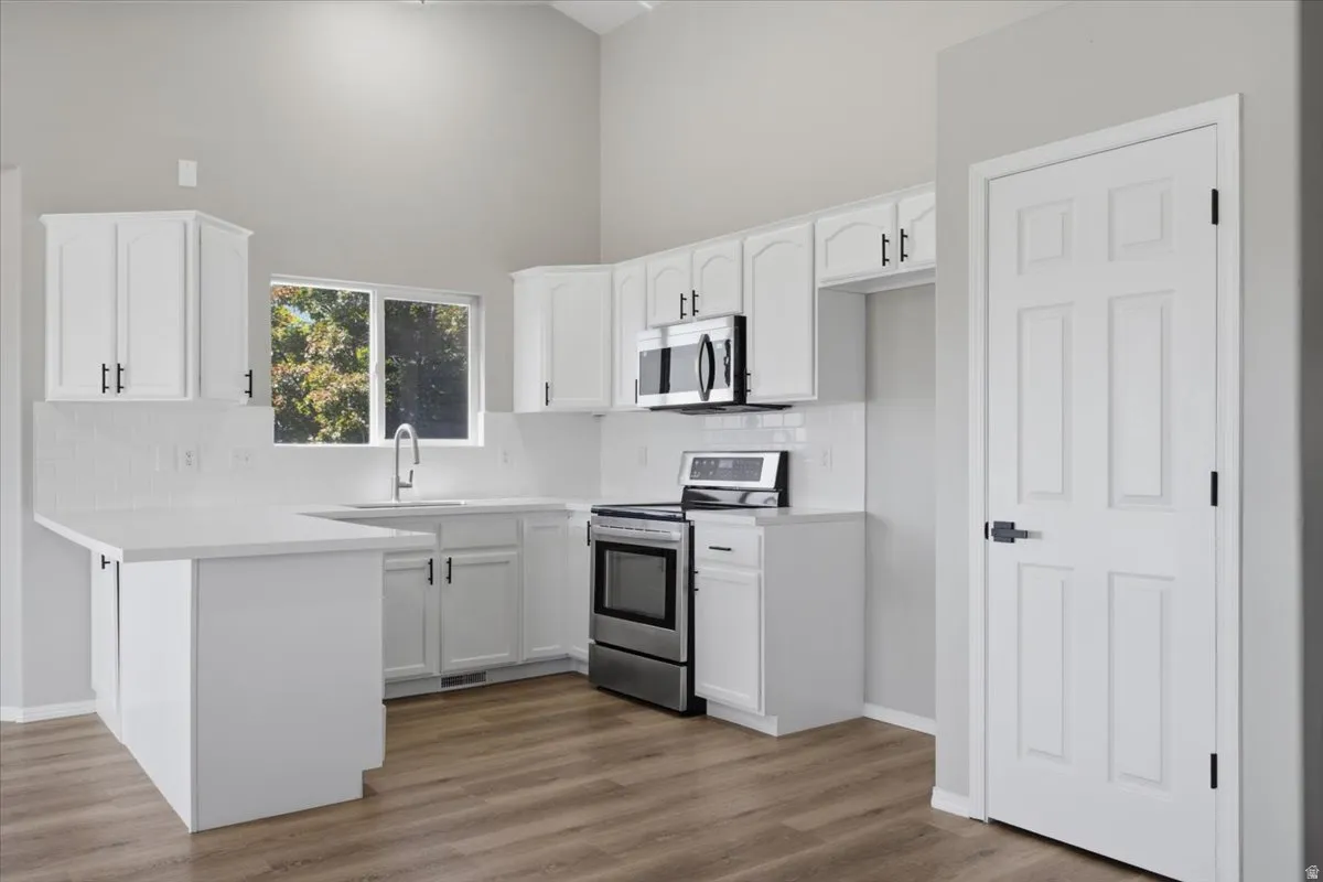 Kitchen featuring vaulted ceilings, white cabinetry with black hardware, stainless steel appliances, a white subway tile backsplash, and wood-finish flooring