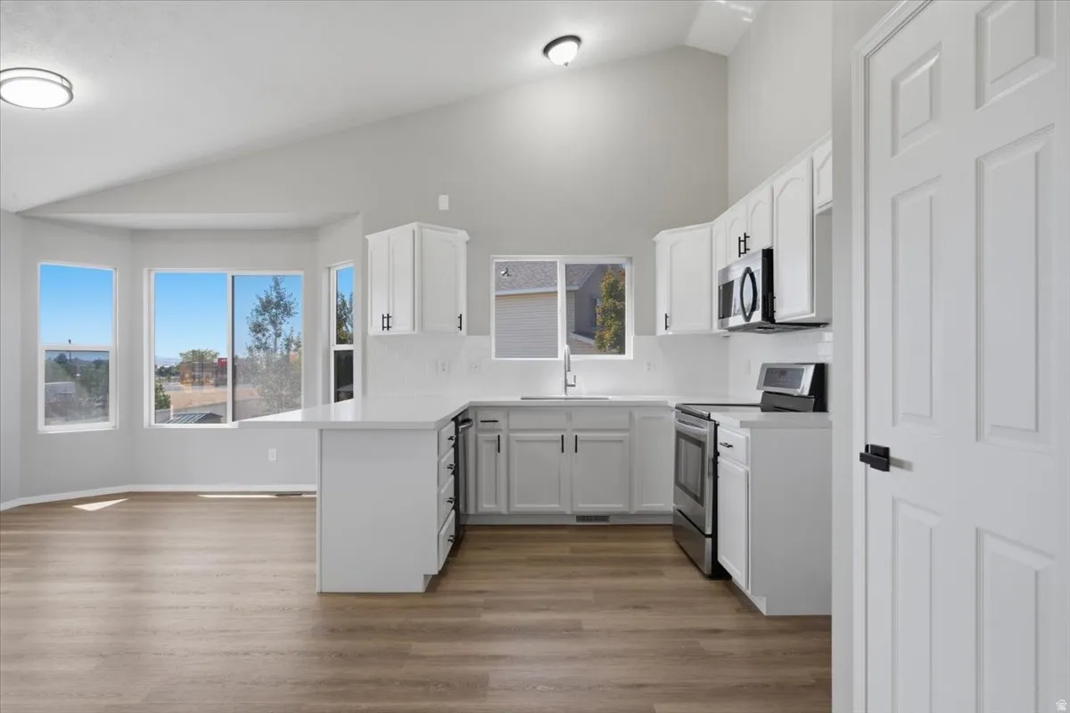 Vaulted ceiling, wood-finish flooring, white cabinetry, integrated stainless steel appliances, and bay windows