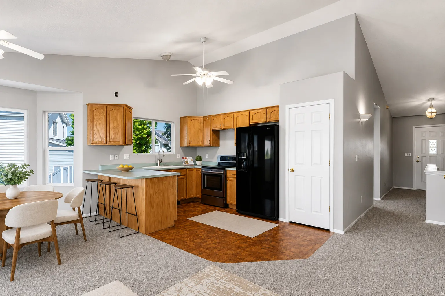 Open-concept kitchen featuring light wood cabinetry, light blue countertops, and a black appliance suite