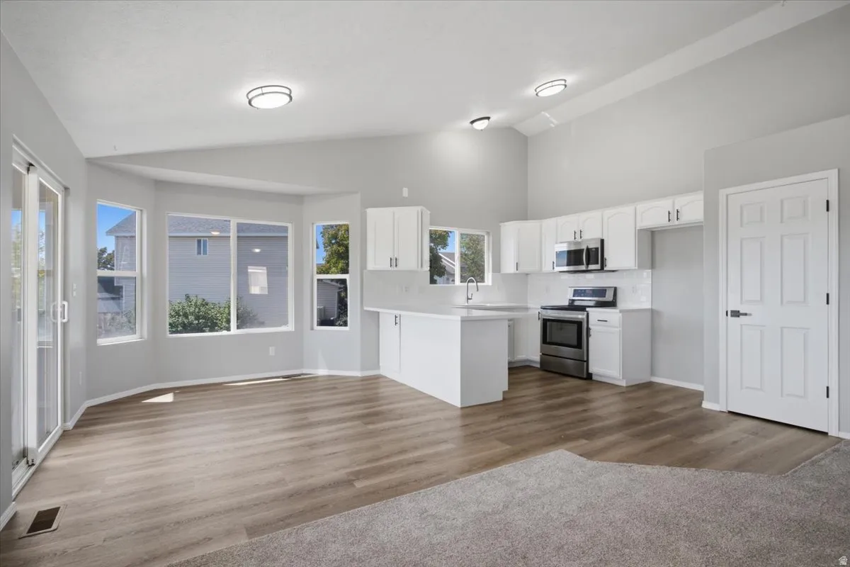 Vaulted ceilings, wood-finish flooring, white cabinetry, stainless steel appliances, and a sliding glass door