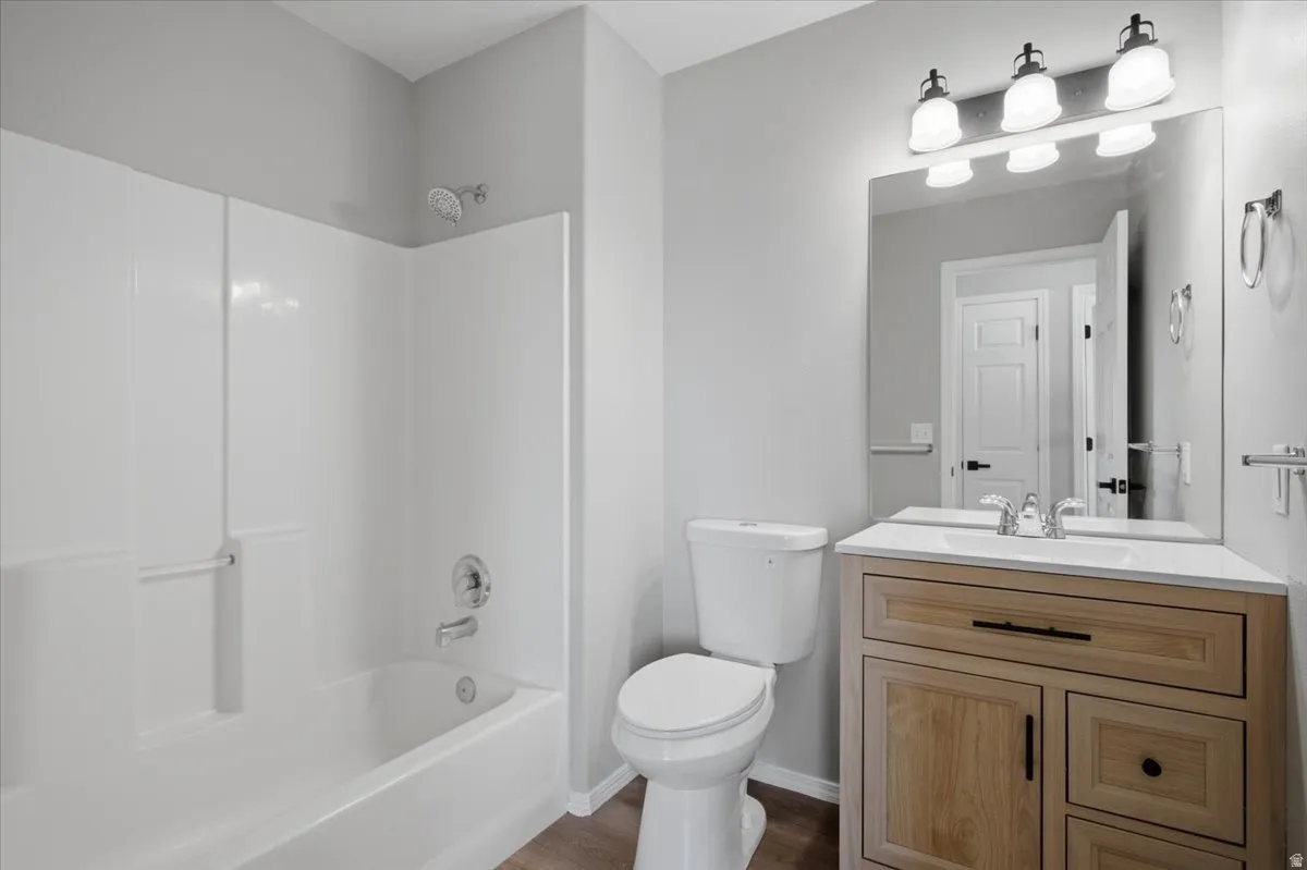 White bathtub with an integrated shower, chrome fixtures, and a light wood-finish vanity with a white countertop