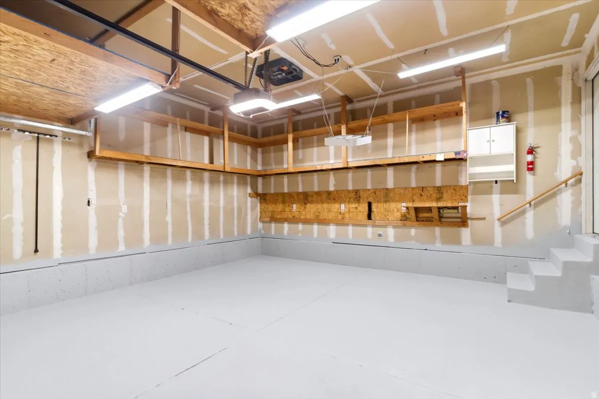 Spacious garage featuring a light gray floor, exposed wood beam ceiling, built-in shelving, and integrated lighting fixtures