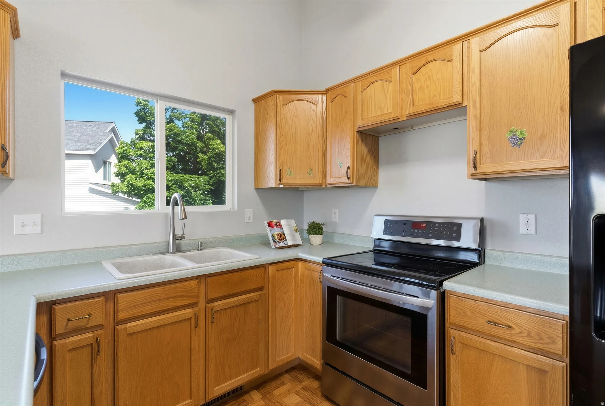 Kitchen featuring oak cabinetry, light-colored countertops, a double basin sink with a high-arc faucet, and stainless-steel appliances including a range and refrigerator