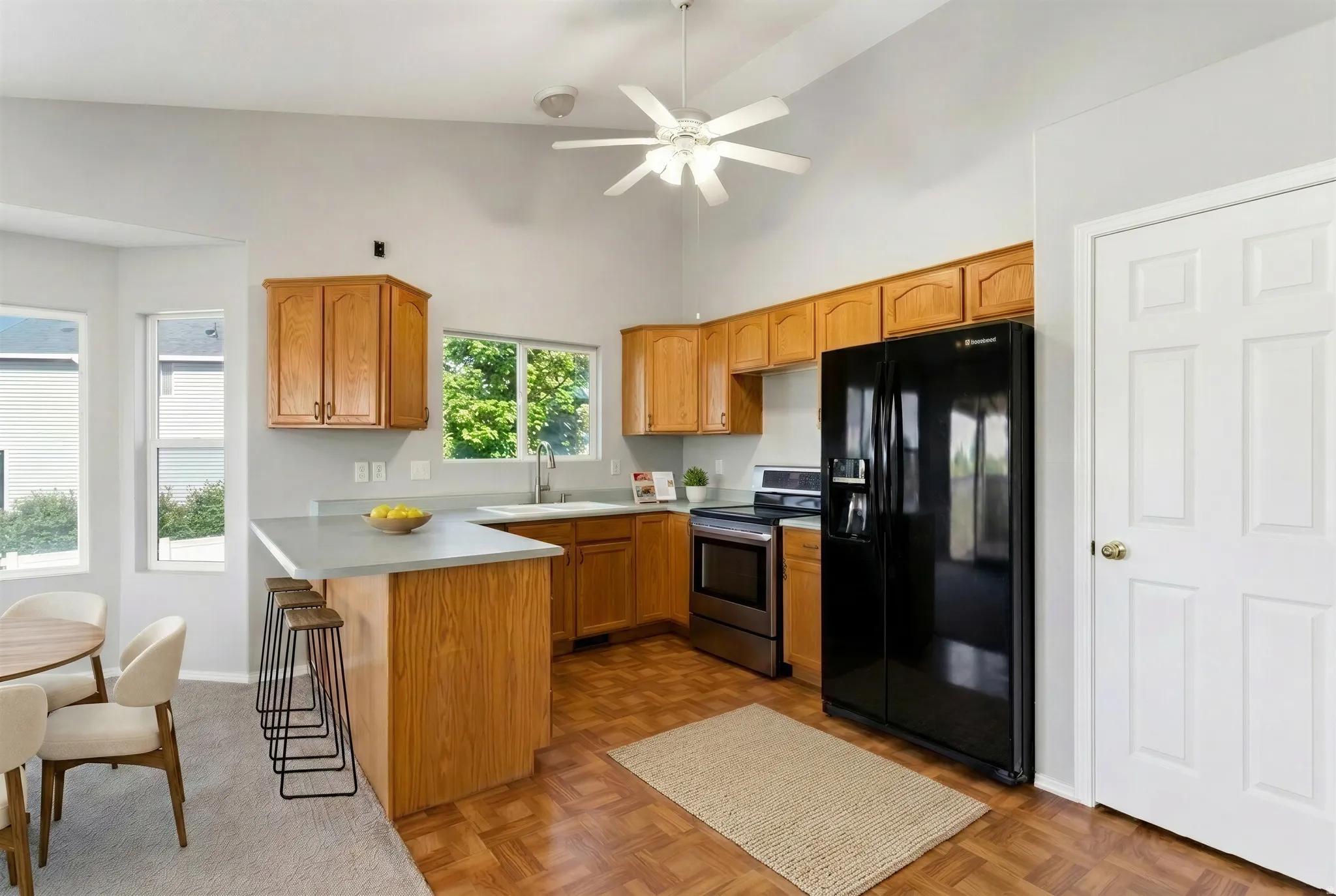 Kitchen featuring a vaulted ceiling with a ceiling fan, light wood-finish cabinetry, stainless steel range, black side-by-side refrigerator, and wood-finish flooring