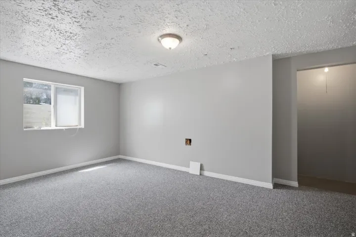 Light gray walls with white baseboards, gray carpet flooring, and a single-pane window