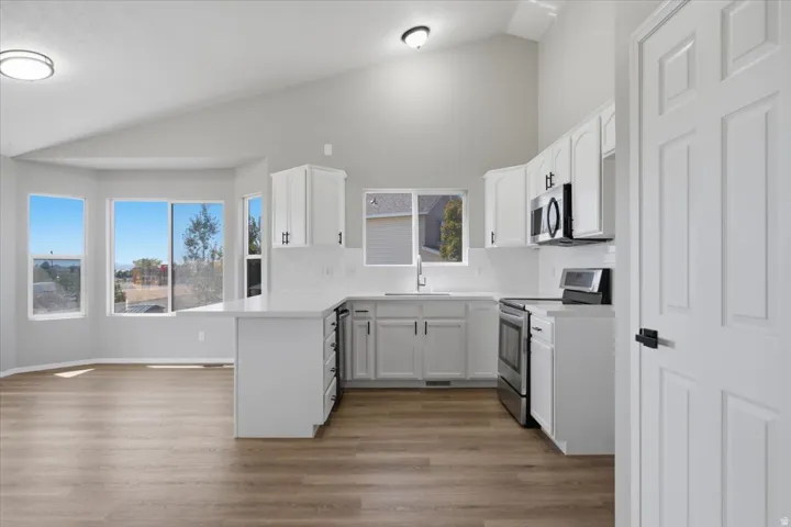 Vaulted ceiling, wood-finish flooring, white cabinetry, integrated stainless steel appliances, and bay windows