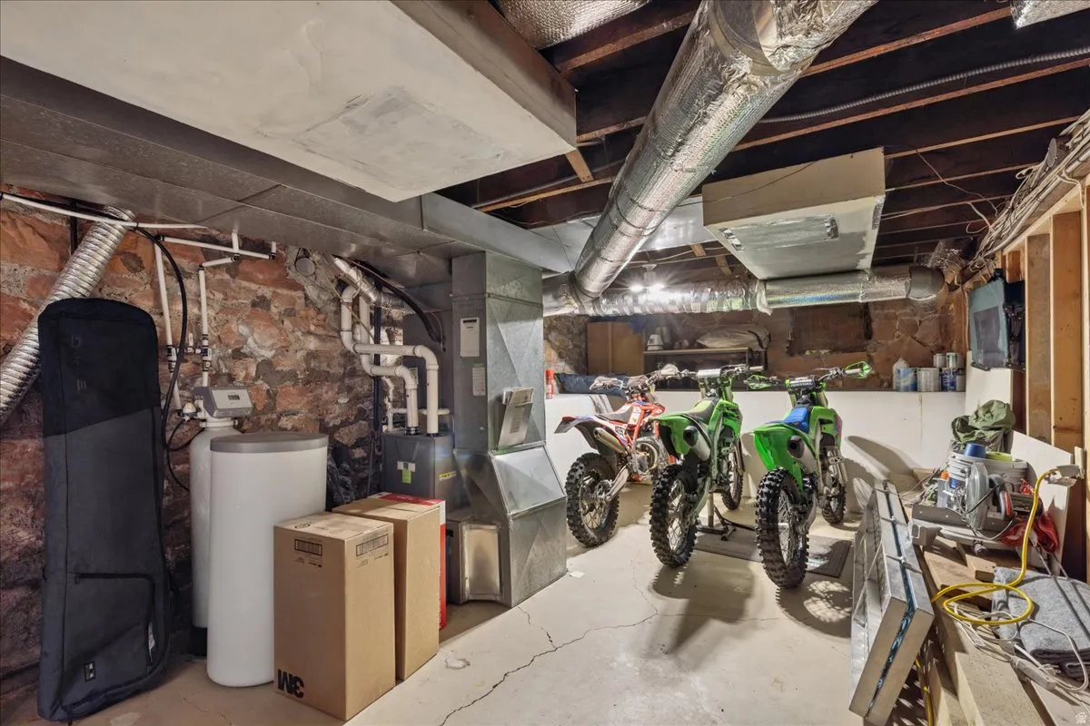 Utility room with exposed stone foundation walls, concrete flooring, and exposed ceiling joists