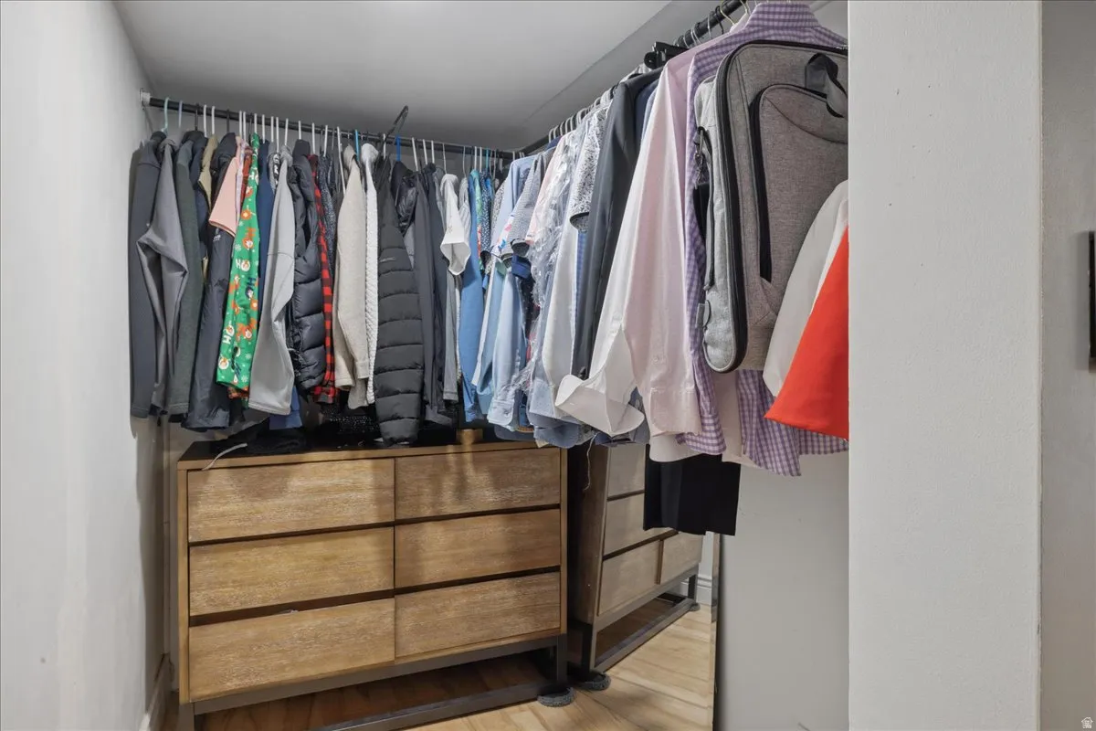 Walk-in closet with integrated wood-finish drawer storage, multiple hanging rods, and a reflective surface
