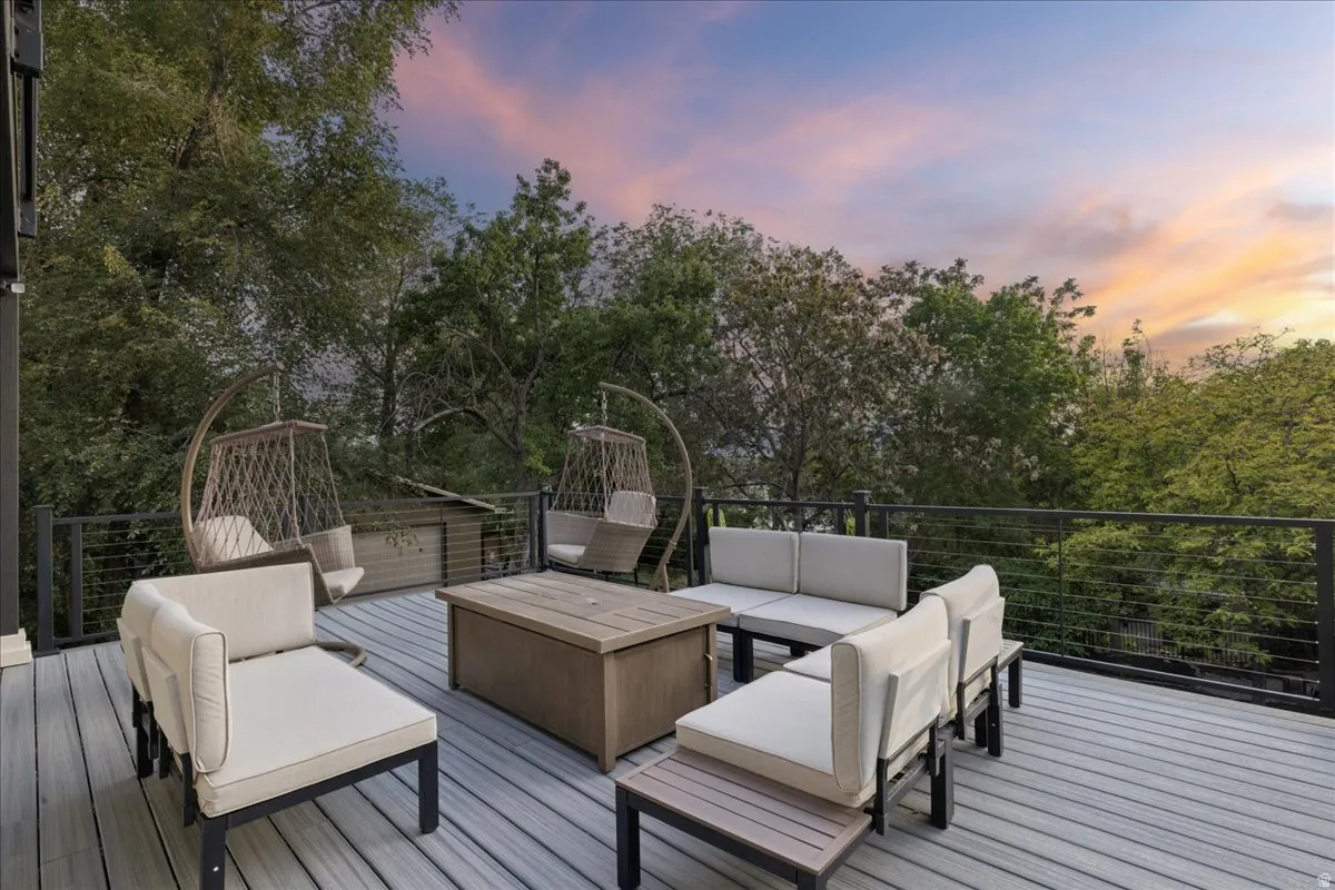 Expansive outdoor deck featuring wood-finish decking, black metal cable railing, and surrounding mature trees