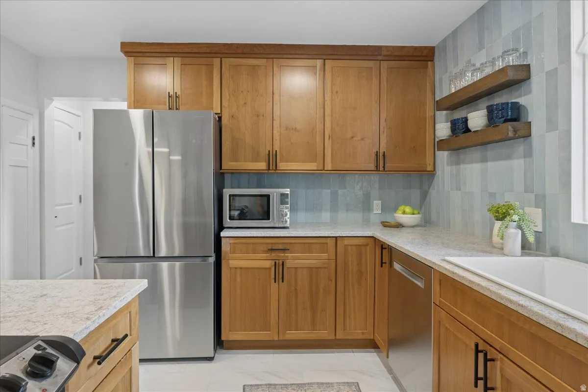 Kitchen featuring wood-finish cabinetry with black hardware, light-toned countertops, a stainless steel French door refrigerator, and an integrated stainless steel dishwasher