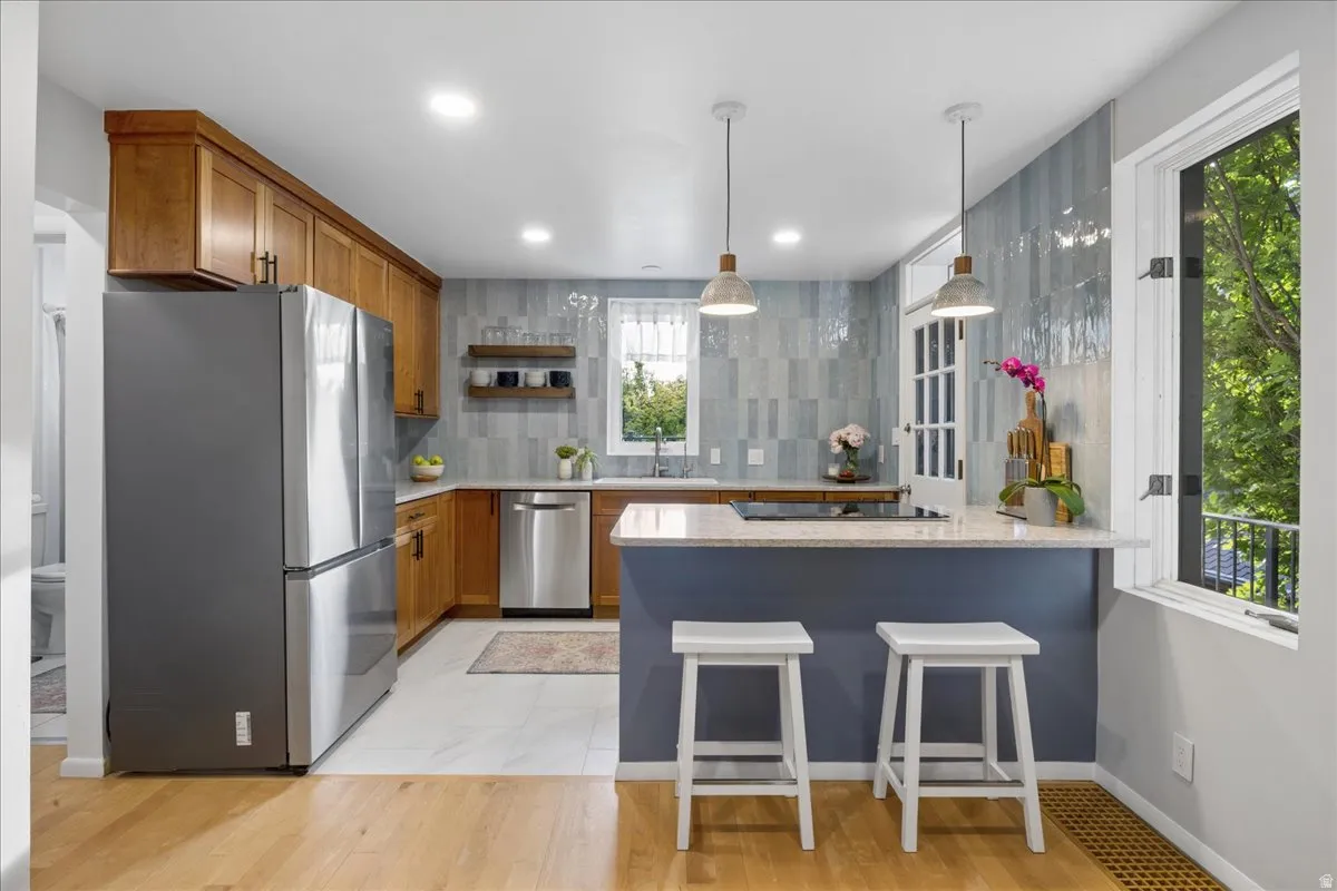Kitchen featuring wood-finish cabinetry, a central island with countertop seating, light-colored countertops, a blue tiled backsplash, and recessed lighting