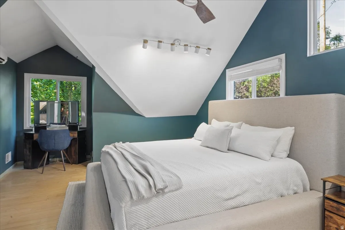 Attic room featuring a sloped ceiling, wood-finish flooring, multiple windows, track lighting, and a ceiling fan