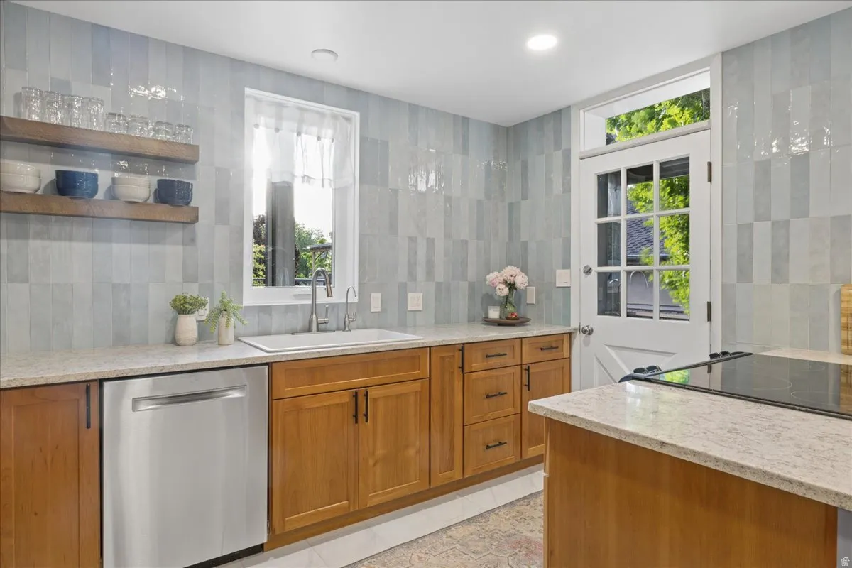 Kitchen featuring light wood cabinetry, light-toned countertops, a stainless steel dishwasher, a white single-basin sink with a gooseneck faucet, and light blue subway tile backsplash