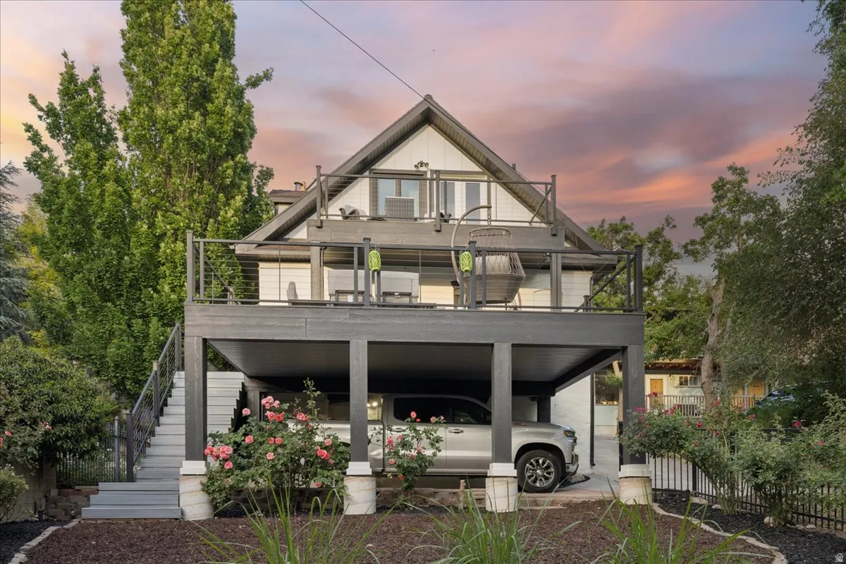 Multi-level residence featuring an elevated deck with wire railing, a lower-level covered parking area, and an exterior staircase with matching wire railing