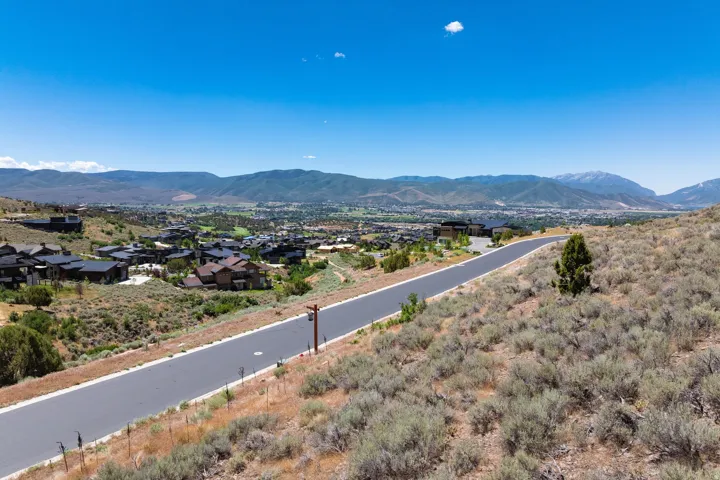 Paved road ascending a natural landscape with distant mountain ranges and scattered residential developments