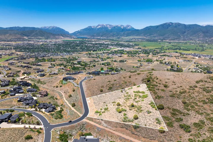 Mountainous terrain backdrop, expansive undeveloped lot, paved road access, scattered natural vegetation, distant residential properties