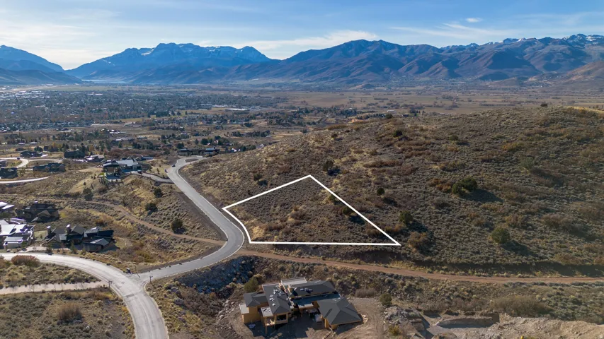 Undeveloped land parcel featuring a curved asphalt road, surrounding natural terrain, and a distant mountain range