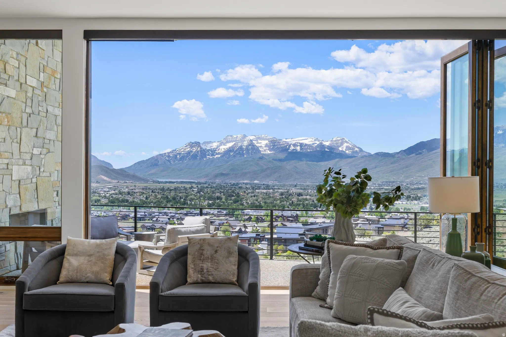 Expansive glass doors open to an outdoor balcony, showcasing a snow-capped mountain backdrop and surrounding landscape