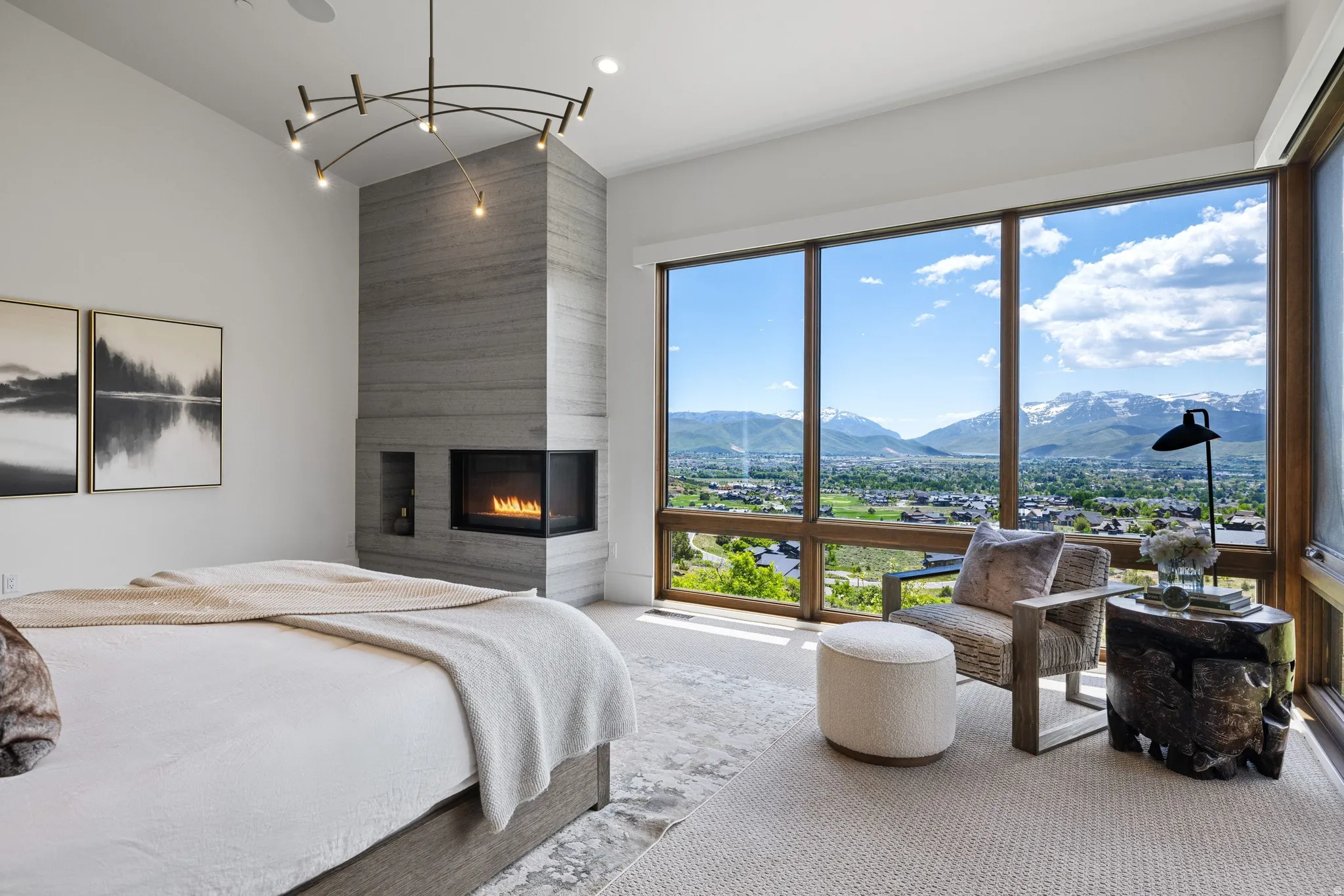 Full-height window wall with natural wood-finish framing, contemporary fireplace with a stone-finish surround, vaulted ceiling, and a modern linear chandelier