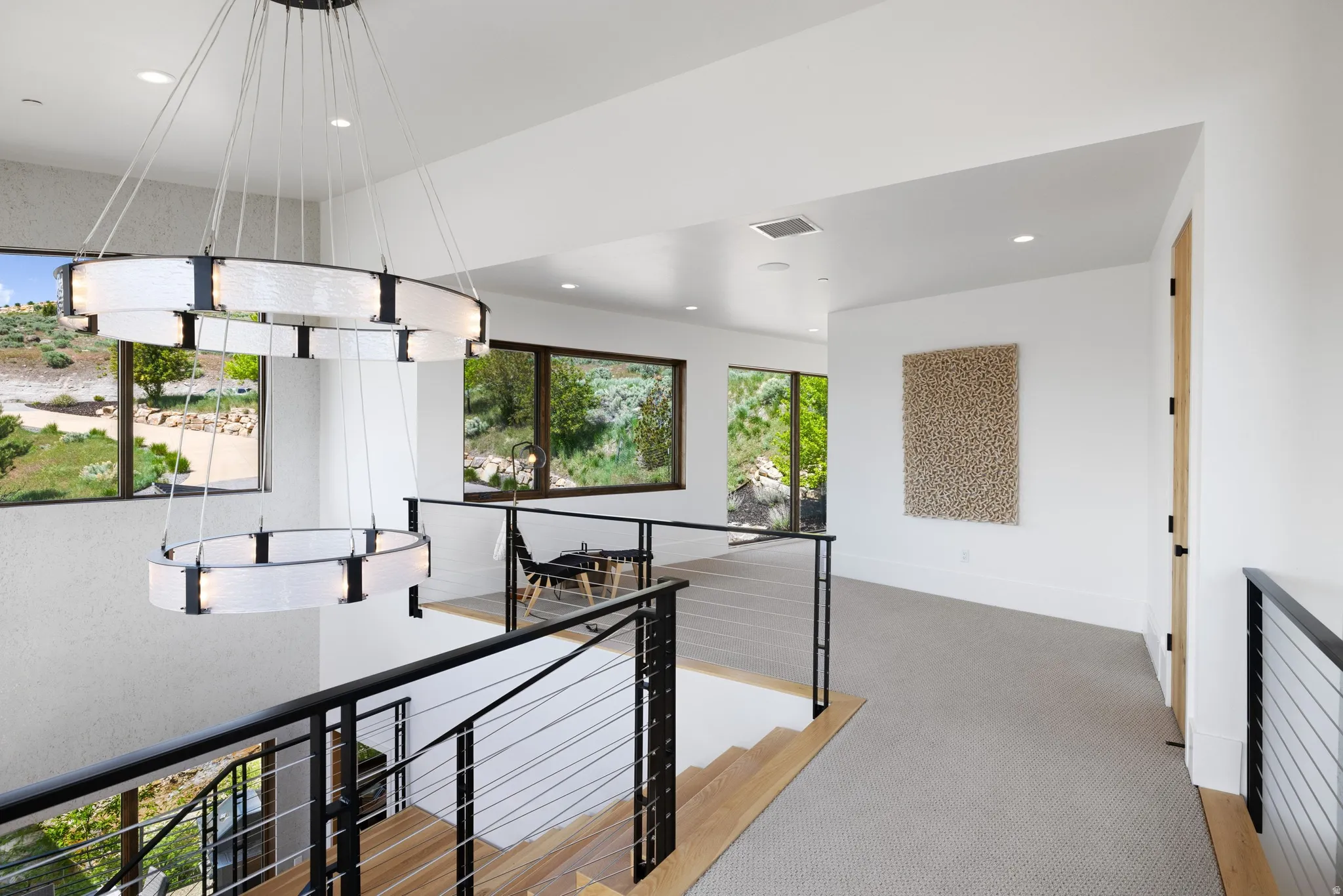 Contemporary two-tiered chandelier illuminating a landing with light wood-finish stairs and cable railing