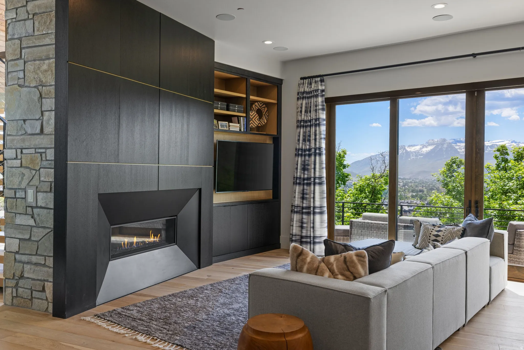 Sleek linear fireplace integrated into custom dark wood cabinetry, complemented by stone accent walls and wide plank wood flooring