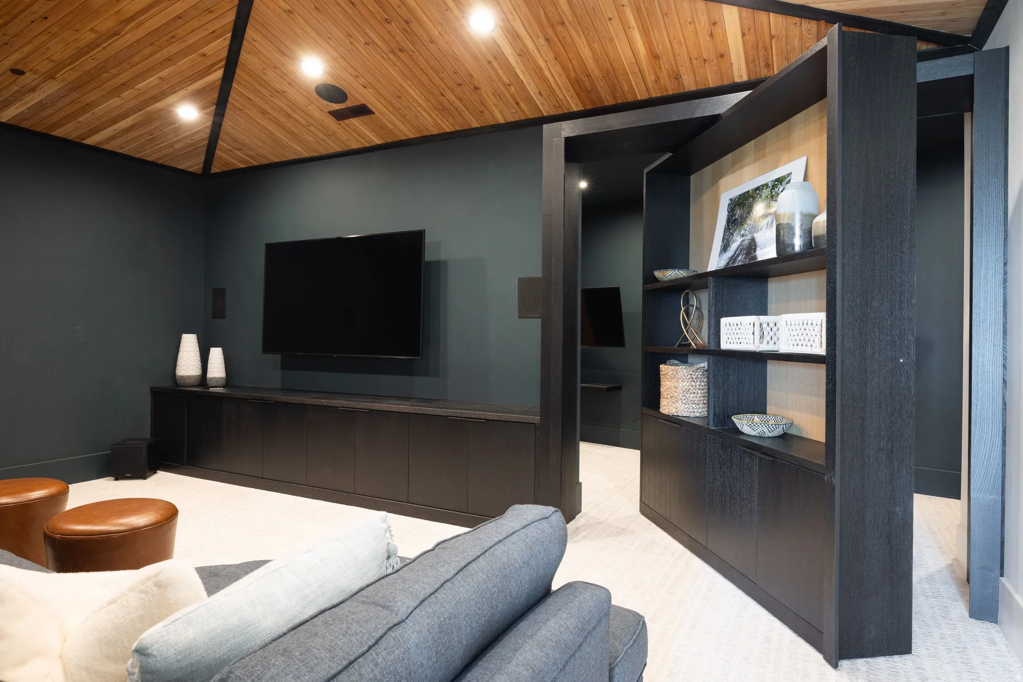 Entertainment room featuring a vaulted wood-paneled ceiling with recessed lighting, dark accent wall, built-in media console, and a pivot bookcase entry