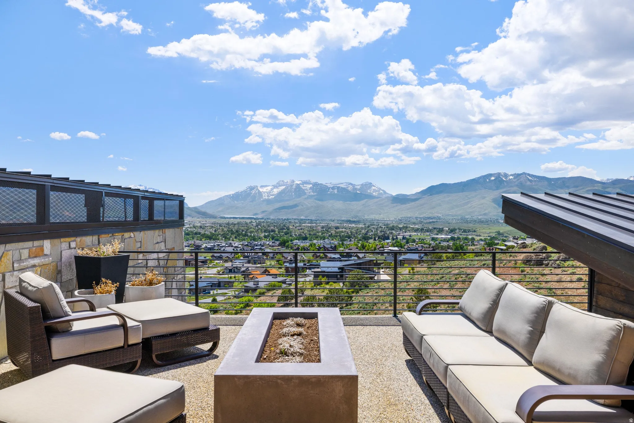Expansive outdoor patio featuring a concrete fire pit, stone wall detailing, and a metal railing