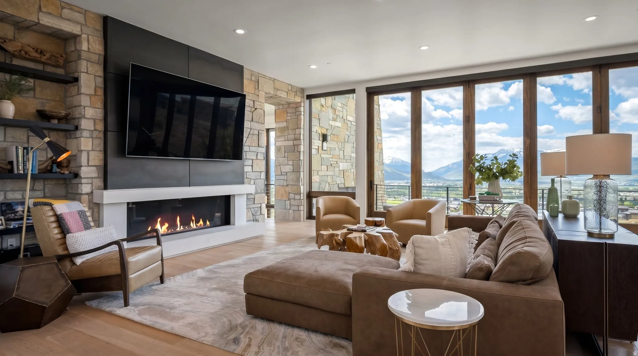 Spacious living area featuring a stone accent wall with built-in shelving, a linear fireplace with a white mantel, an integrated television mount, light wood-finish flooring, and large picture windows