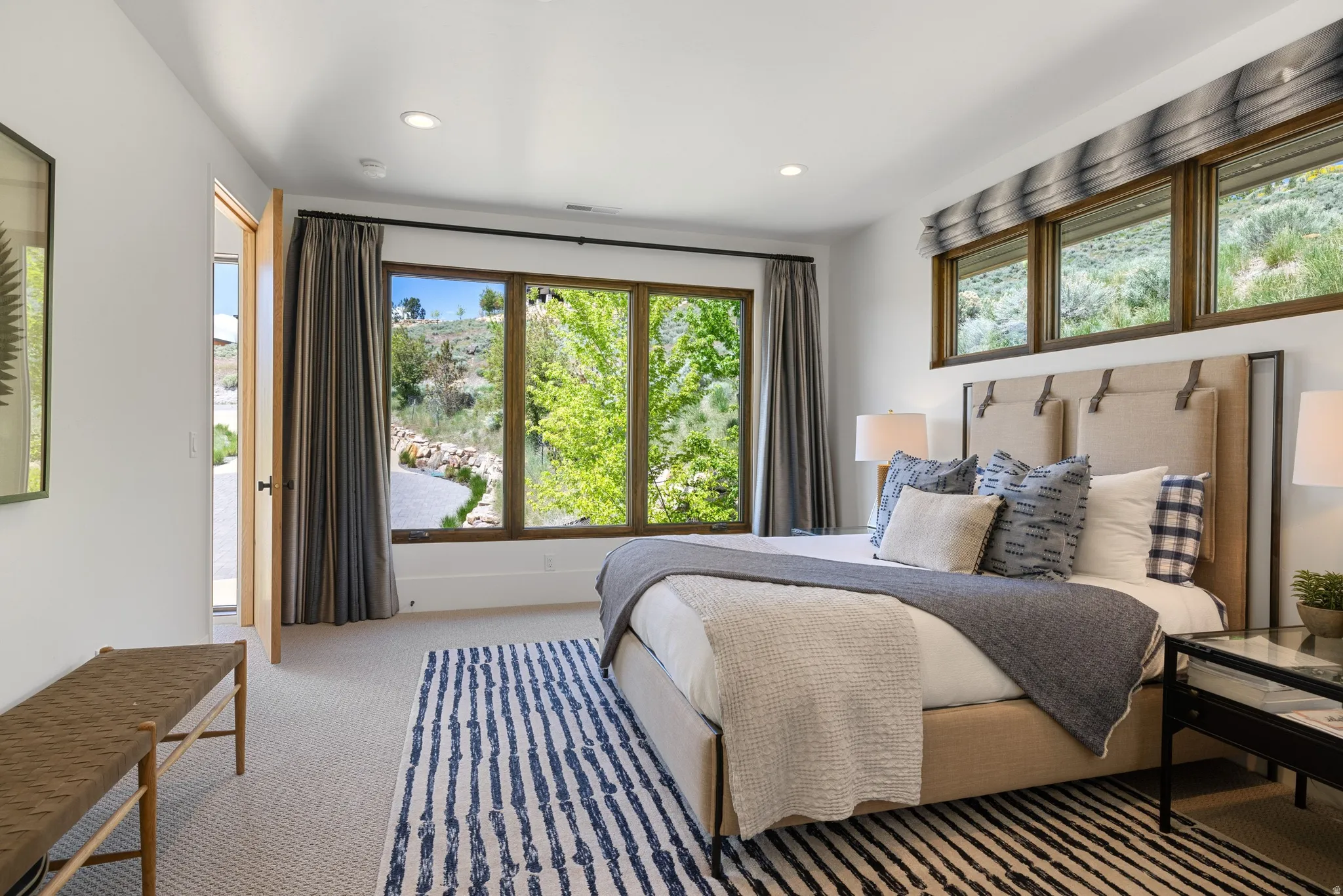 Spacious bedroom featuring large windows, light-toned carpeting, recessed lighting, a neutral-toned upholstered headboard, and a natural wood-finish door