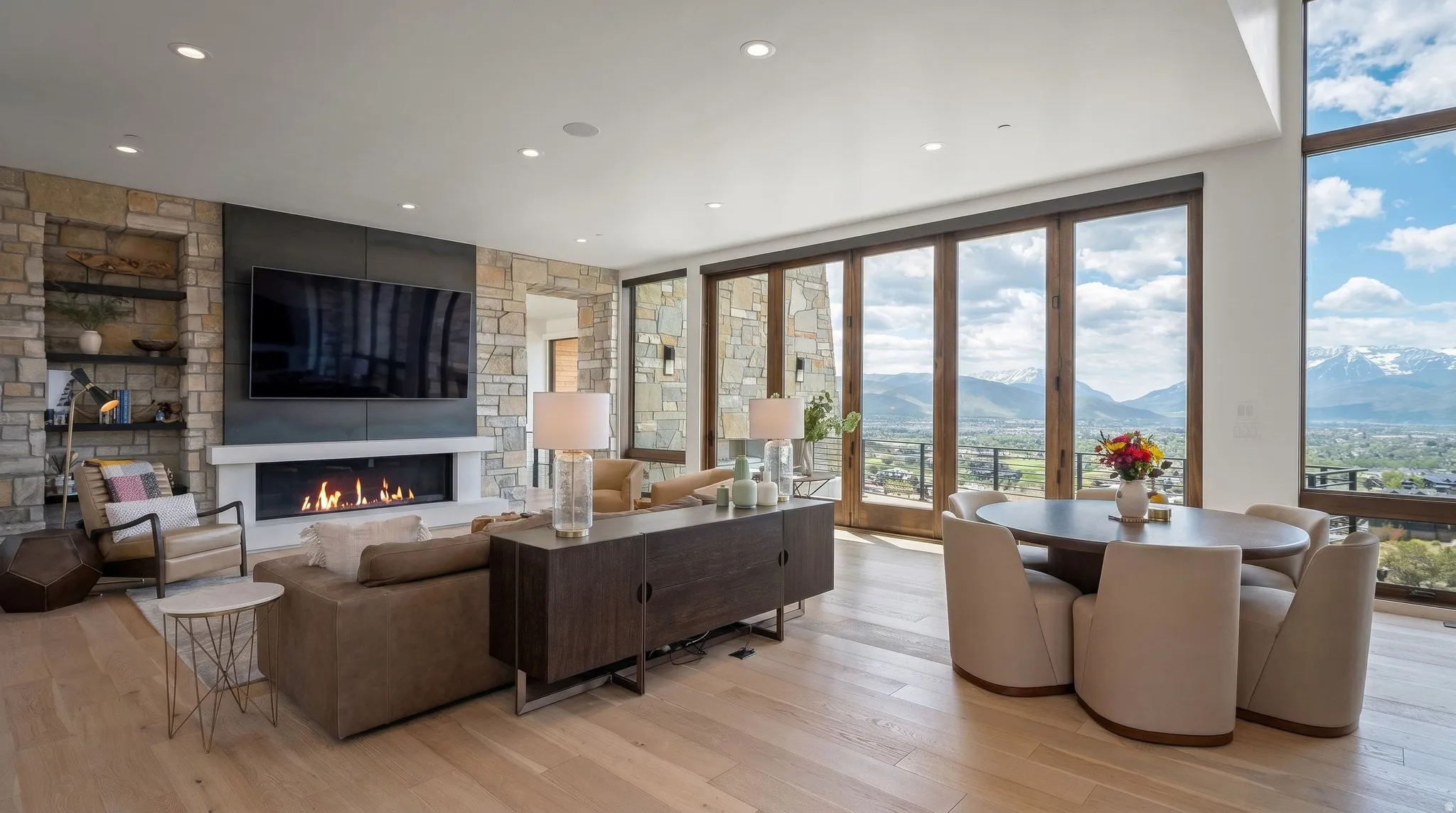Open-concept living space with light wood-finish flooring, a stone-accented wall, and a linear fireplace