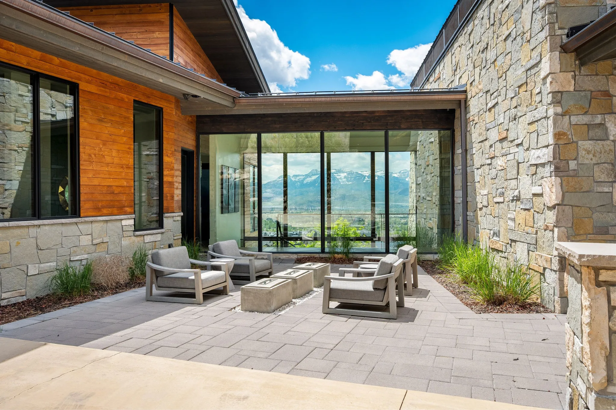 Exterior patio with paver flooring, featuring a glass-enclosed interior space, stone exterior facade, wood-panel siding, and black-framed windows