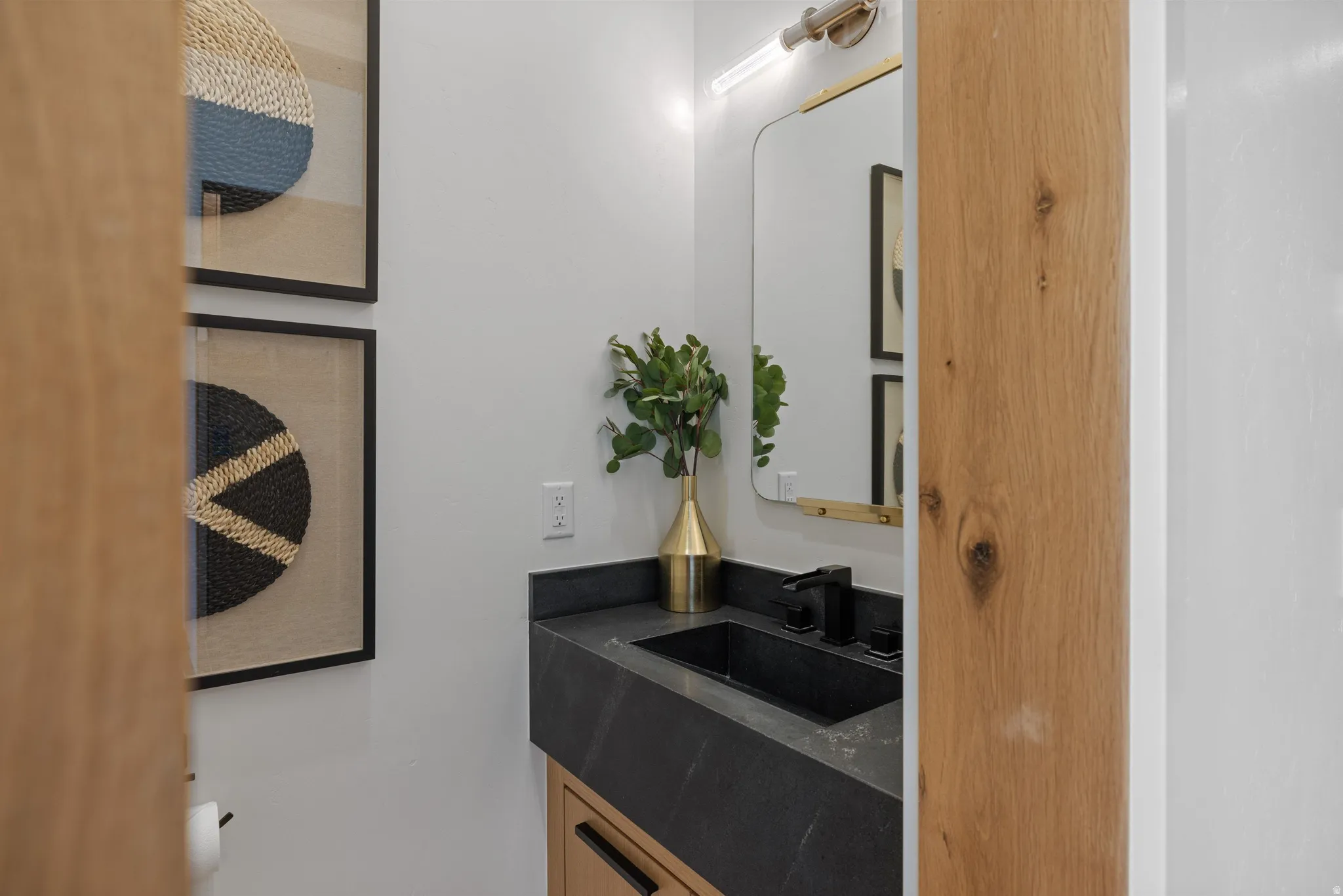 Vanity featuring a dark countertop with an integrated sink, matte black faucet, and brass-framed mirror