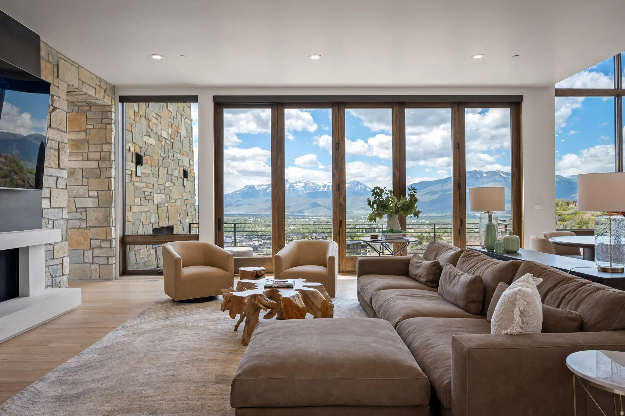 Expansive living space featuring a floor-to-ceiling stone fireplace, wood-finish flooring, and large bi-fold glass doors