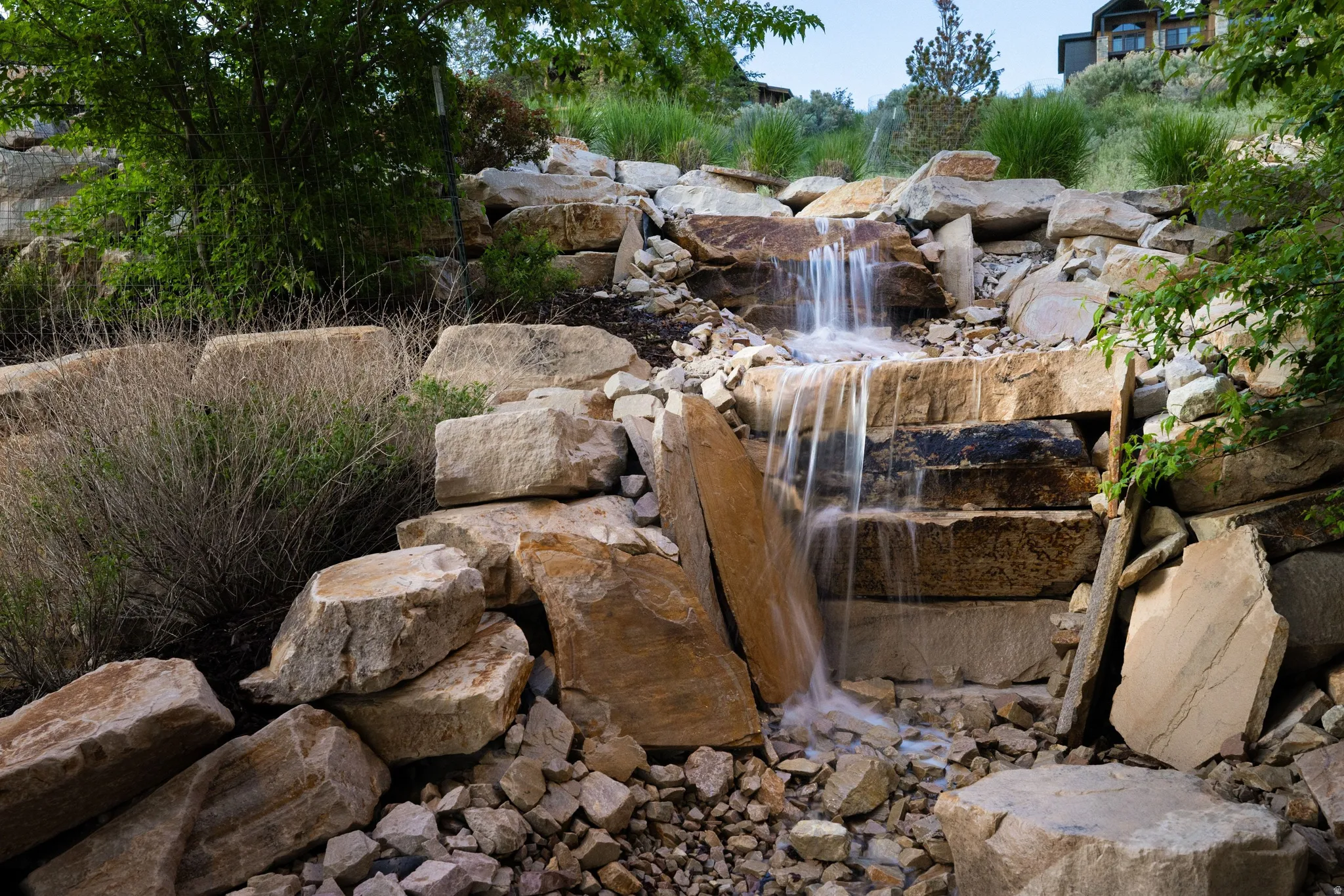 Tiered rock waterfall feature with natural stone landscaping, integrated into a sloped terrain