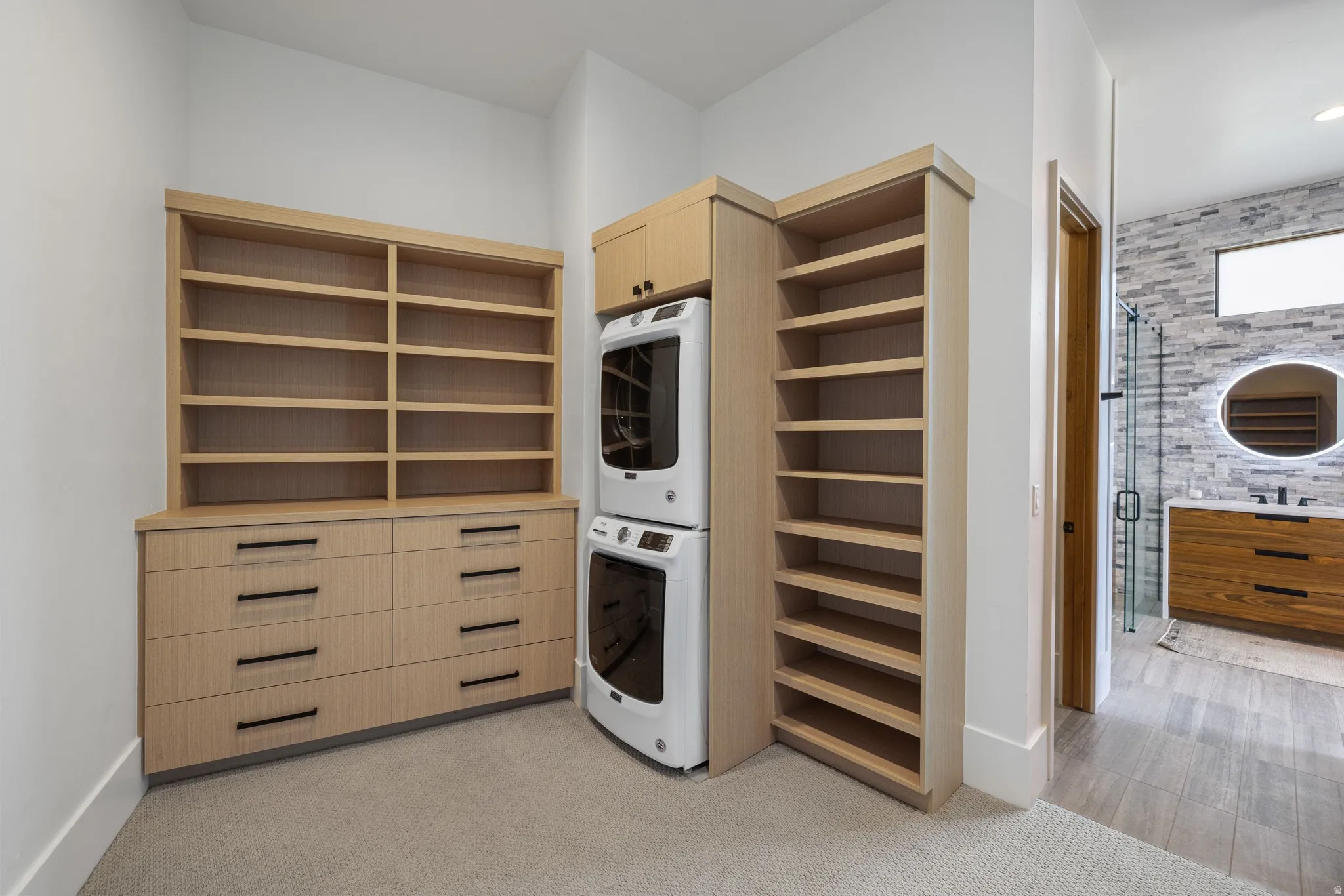 Custom built-in cabinetry with extensive shelving and storage drawers, wood-finish flooring, and a stackable washer and dryer unit