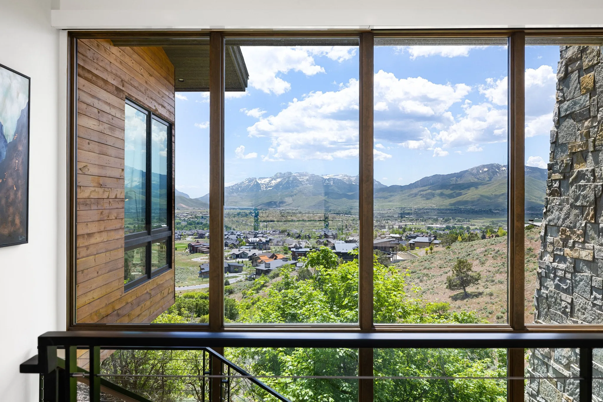 Floor-to-ceiling window system with dark wood-finish framing, integrated into natural stone and horizontal wood siding